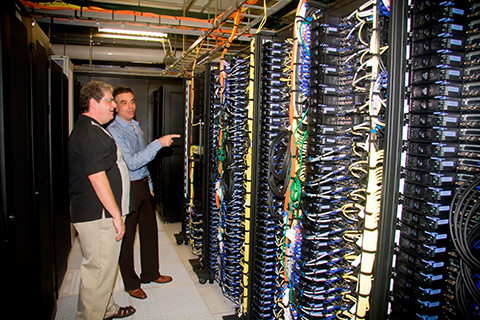 Two people stand in front of the University of Miami supercomputer on campus. 