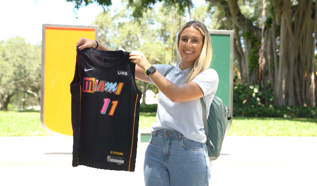 Giovanna Boutris Paschoalin holds up her Miami Heat jersey in front of the U sculpture. 